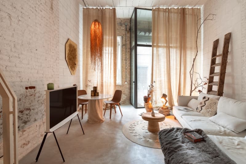 White brick living room with off white sofa, stone floor, large windows, and lots of neutral and warm tones