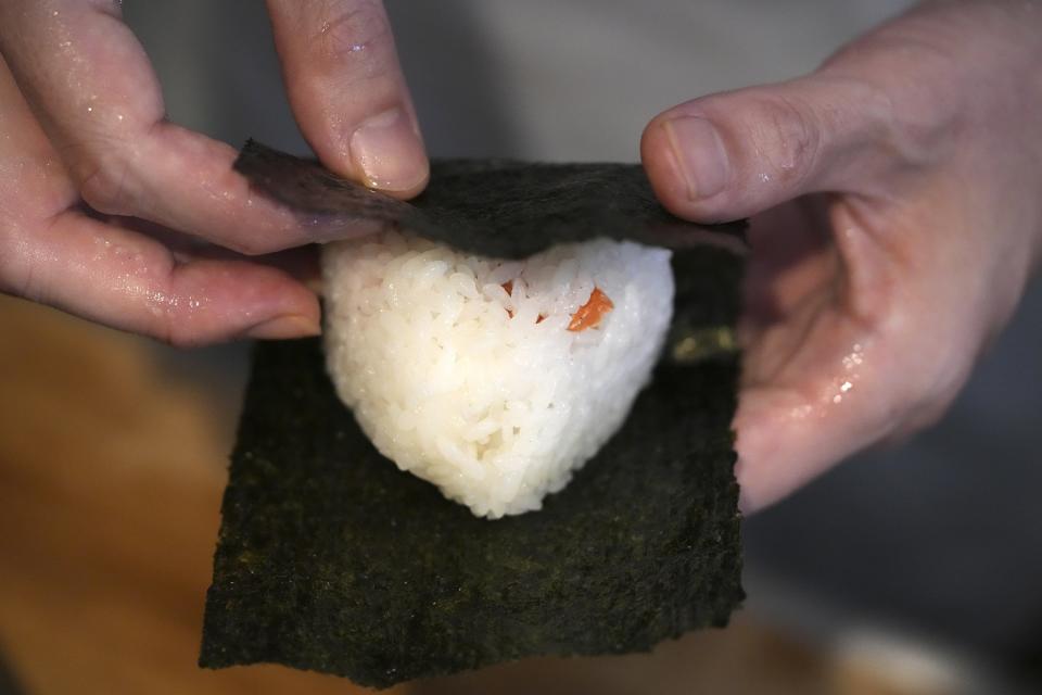 Yosuke Miura wraps seaweed around a rice ball at Onigiri Asakusa Yadoroku, Tokyo's oldest onigiri restaurant, on June 3, 2024, in Tokyo. The word "onigiri" just became part of the Oxford English Dictionary this year. The humble sticky-rice ball, a mainstay of Japanese food, has entered the global lexicon. (AP Photo/Eugene Hoshiko)