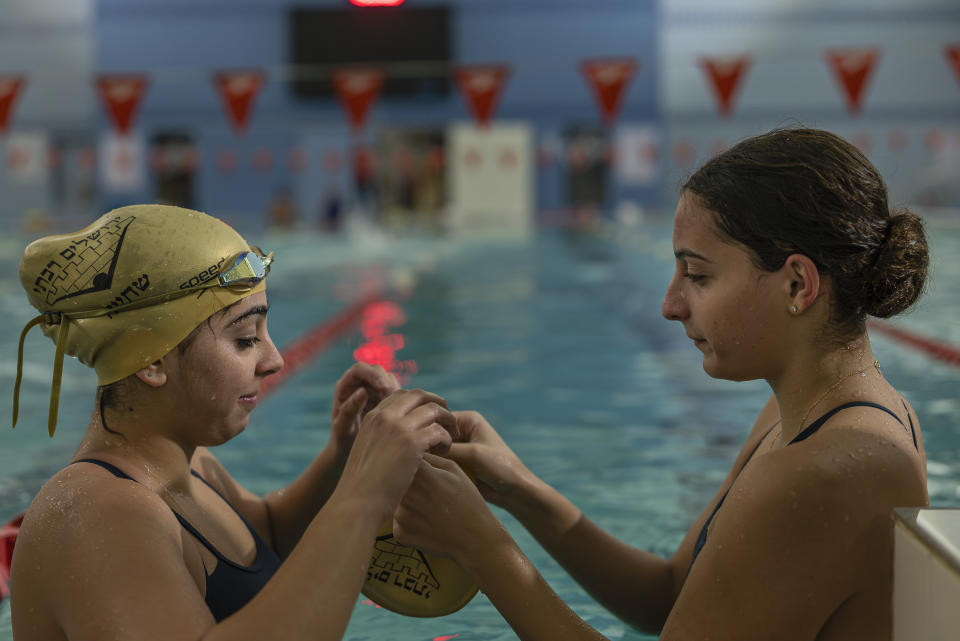 Shira Chuna, a la izquierda, y Avishag Ozeri, nadadoras del club de natación Gran Jerusalén, cuyos miembros son israelíes y palestinos, se ayudan la una a la otra con su equipamiento de natación en una piscina de la YMCA en Jerusalén, el 5 de noviembre de 2023. (Afif H. Amireh/The New York Times).