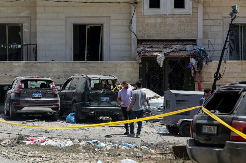 Supporters of Pro-Iranian Hezbollah stand in front of destroyed cars and a building that was heavily hit when Israeli warplanes raided overnight a nearby three-story in the southern Lebanese village of Janata, where at least one person was killed and more than seven others wounded. Marwan Naamani/dpa