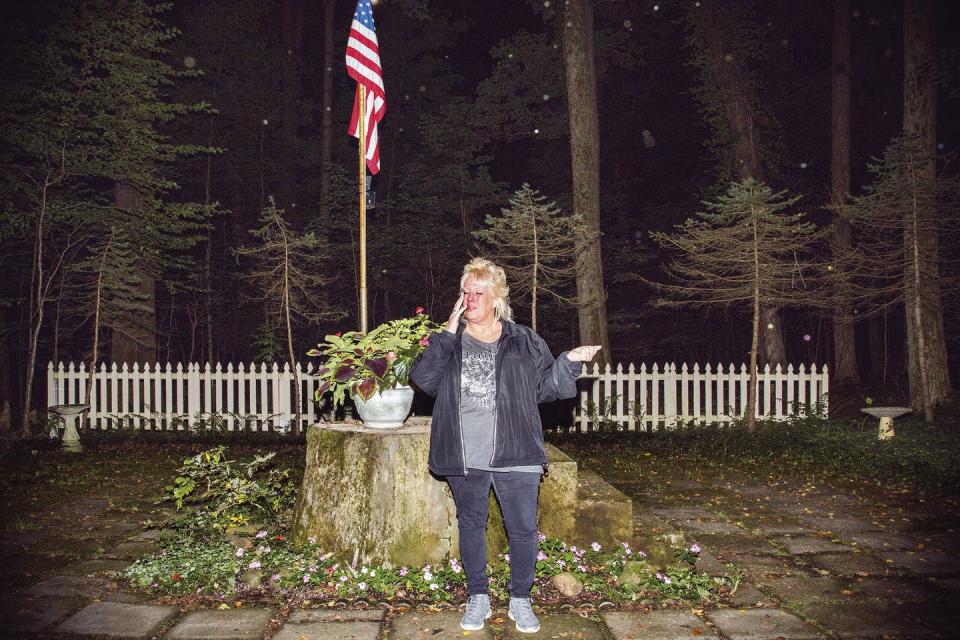 Woman stands before American flag with arms outstretched.