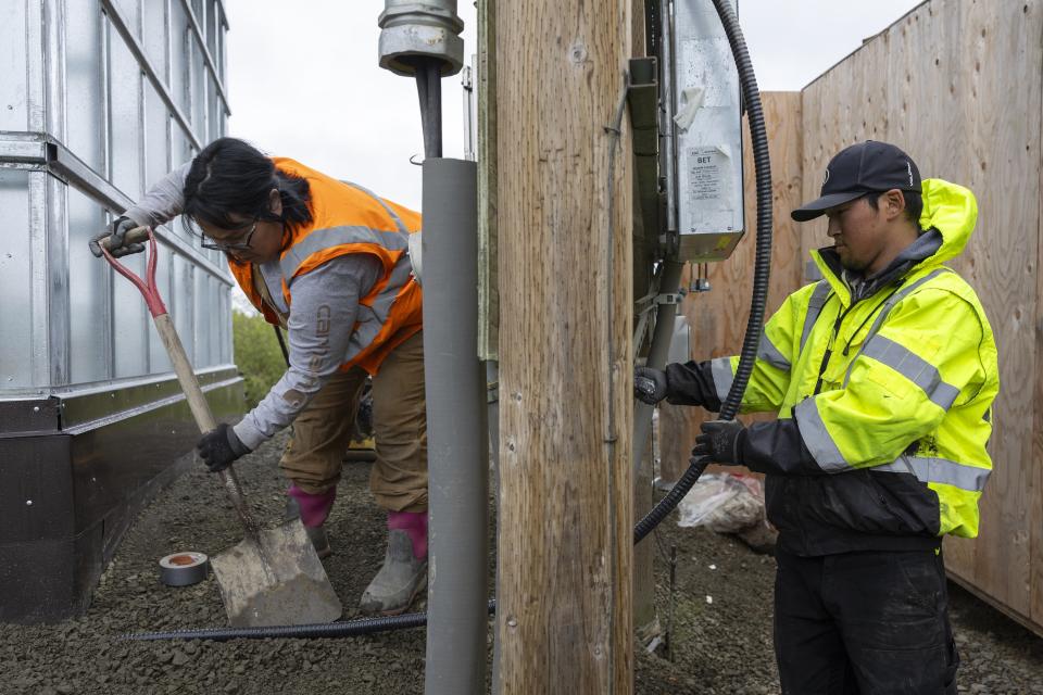 Alaska Native Tribal Health Consortium staff Darlene Ayapan, left, uses a shovel as Terrance Ekamrak installs a power supply cable to a newly developed lift house, Thursday, Aug. 17, 2023, in Akiachak, Alaska. Most of the village's nearly 700 people are getting modern plumbing for the first time this spring and summer — and finding their lives transformed. (AP Photo/Tom Brenner)