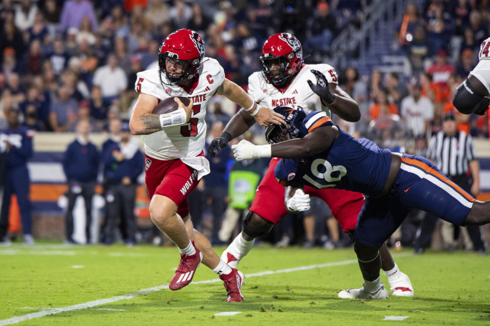 North Carolina State quarterback Brennan Armstrong (5) escapes the grasp of Virginia defensive tackle Michael Diatta (18) during the first half of an NCAA college football game Friday, Sept. 22, 2023, in Charlottesville, Va. (AP Photo/Mike Caudill)