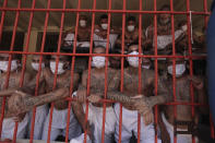 Imprisoned gang members, wearing protective face masks, look out from behind bars during a media tour of the prison in Quezaltepeque, El Salvador, Friday, Sept. 4, 2020. President Nayib Bukele denied a report Friday that his government has been negotiating with one of the country’s most powerful gangs to lower the murder rate and win their support in mid-term elections in exchange for prison privileges. (AP Photo/Salvador Melendez)