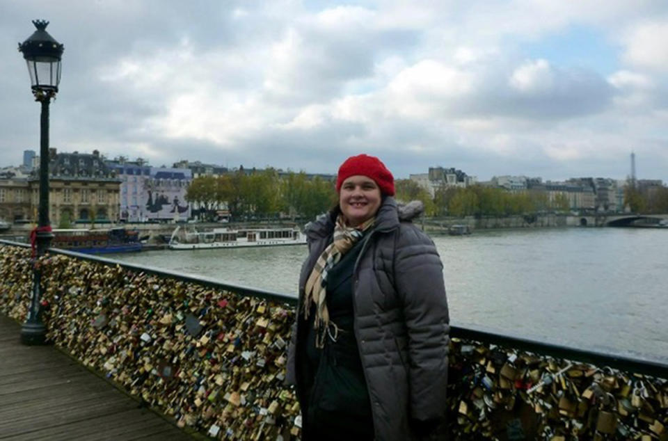 A photo of Sydney woman Maria wearing a grey coat and red beanie on a bridge covered in locks