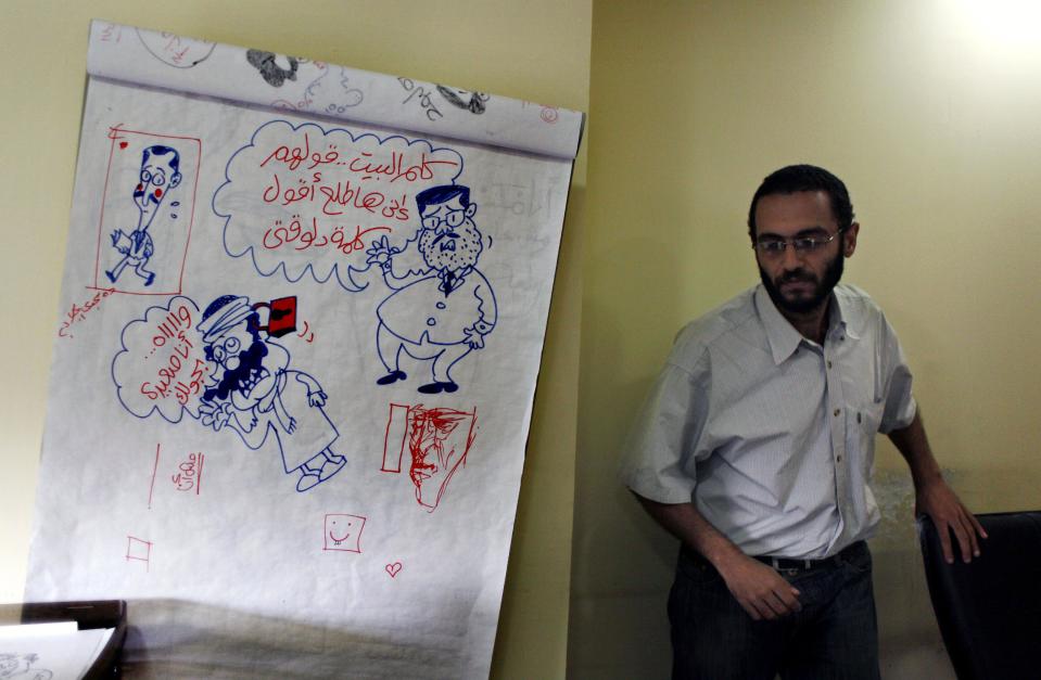 Egyptian cartoonist Abdul-Rahman Najmuddin walks past cartoon sketches, one depicting Egyptian president Mohammed Morsi with a caption in Arabic "someone calls home and tell them that I am delivering a speech," at his office in the Egyptian Al Watan daily newspaper headquarters in Cairo, Egypt, Wednesday, Sept. 26, 2012. Amid outrage sparked by perceived insults to Islam, one Egyptian newspaper has decided to fight cartoons with cartoons. Al Watan daily says it is responding to the crude caricatures published last week by a satirical Parisian weekly in kind: a series of sketches critiquing relations between the Arab world and the West. The paper says they are a “civilized” alternative to the violent protests across the Muslim world sparked by a low-budget anti-Islam film produced in the United States. (AP Photo/Nasser Nasser)