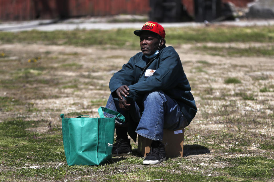 In this Tuesday, May 12, 2020, photo, Manson Gibson sits with his box and bag of food as he waits for a ride home at a giveaway sponsored by the Greater Chicago Food Depository in the Auburn Gresham neighborhood of Chicago. Across the country, food insecurity is adding to the anxiety of millions of people, according to a new survey that finds 37 percent of unemployed Americans ran out of food in the past month, while 46 percent worried that they would. The nationwide unemployment rate on Friday was 14.7 percent, the highest since the Great Depression.(AP Photo/Charles Rex Arbogast)