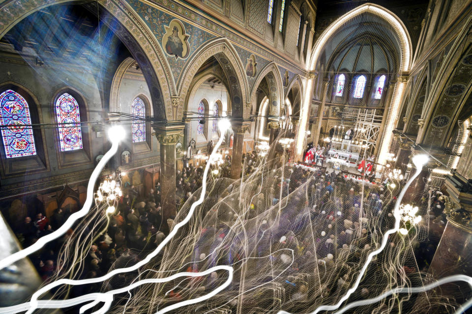 FILE - In this March 24, 2013 file photograph taken with a long exposure, Romanian Catholic worshipers attend a Palm Sunday religious service at the St. Joseph cathedral in Bucharest, Romania. Bucharest enjoys a rich multi-faith tradition, revived since 1989, with synagogues, mosques, and Romanian Orthodox churches in every neighborhood. It was founded by a shepherd, according to local legend, and was later nicknamed the Paris of the East. But Bucharest's idyllic roots and elegant reputation eventually gave way to a series of 20th century calamities: war, invasions, earthquakes and communism.(AP Photo/Vadim Ghirda, File)