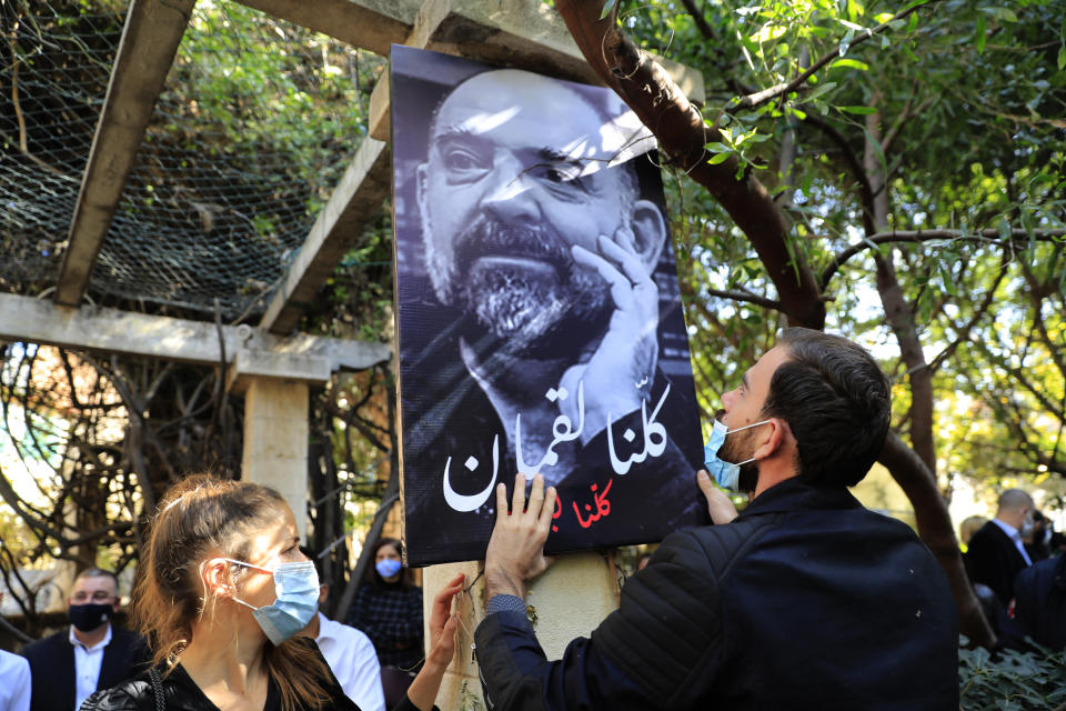 An activist friend of Lokman Slim hangs a portrait of Slim with Arabic reading "We are all Lokman," during a memorial service to pay tribute to the slain Lebanese publisher and vocal critic of Hezbollah group in the southern suburb of Beirut, Lebanon, Thursday, Feb. 11, 2021. Scores of friends and family members bid Slim farewell Thursday in a ceremony attended by western diplomats and organized in his home in the southern suburb of Beirut amid tight security. (AP Photo/Hussein Malla)