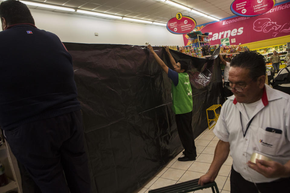 Workers of a supermarket place a black canvas over stacked alcoholic drinks, which the electoral law prohibits selling one day before the general elections, in Guatemala City, Saturday, June 15, 2019. Polls favor former first lady Sandra Torres of the National Unity and Hope party to finish first, but with 19 candidates in the race it is unlikely she will win the absolute majority necessary to avoid a runoff. (AP Photo/Oliver de Ros)