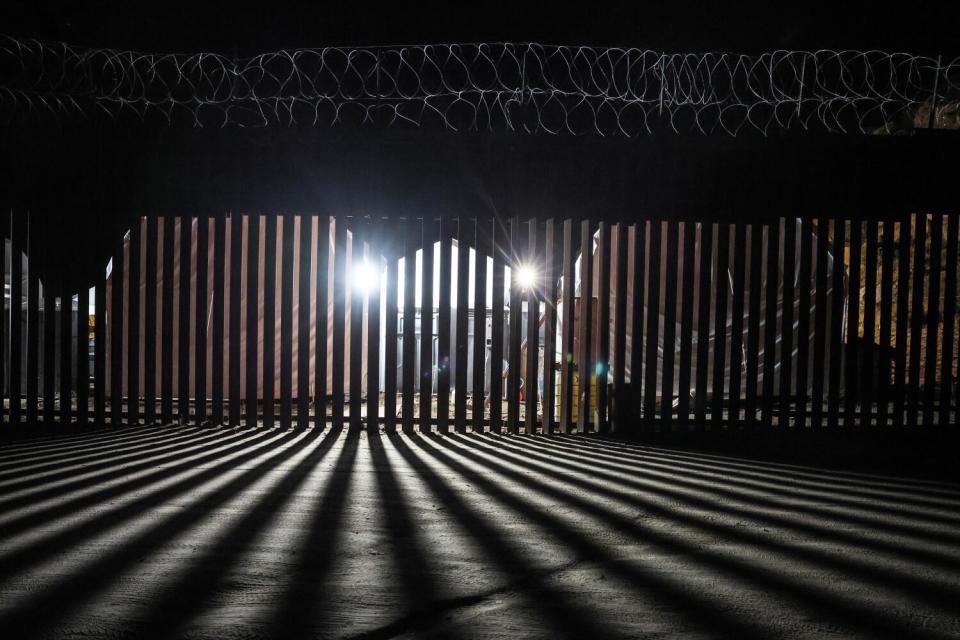 Light shines through vertical slats of a fence at night.