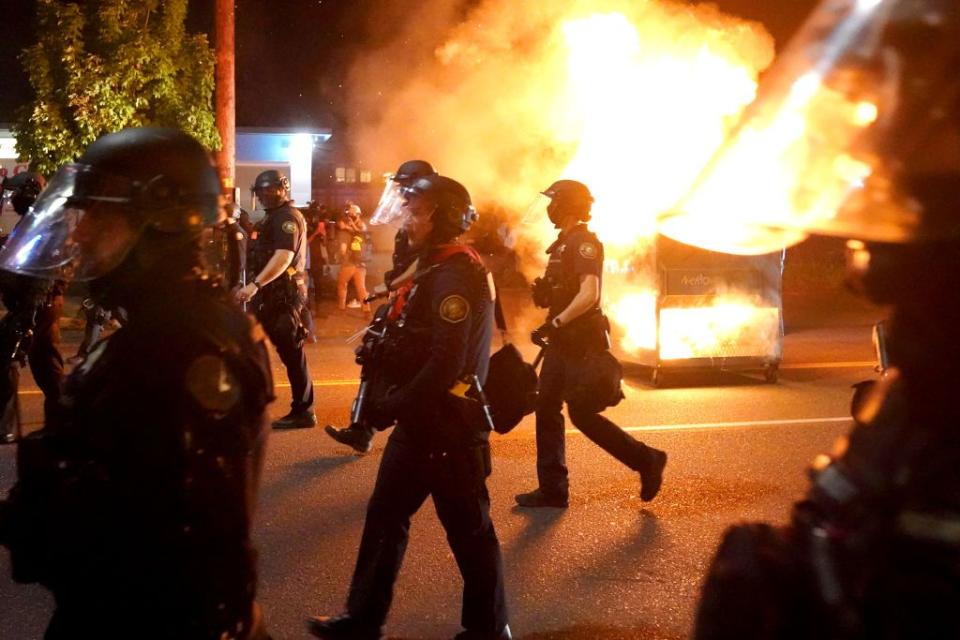 La policía de Portland pasa junto a un contenedor de basura incendiado mientras dispersa la manifestación, el 14 de agosto de 2020 en Portland, Oregón. Fuente: Getty