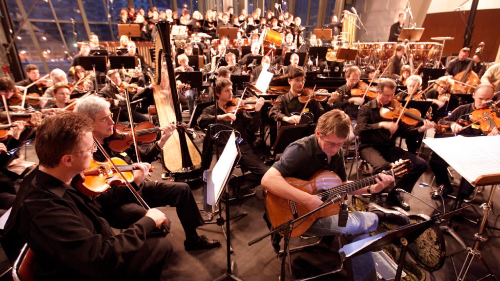 Mike Oldfield (with guitar) performs with the Music Of The Spheres orchestra | Credit: Jasper Juinen/Getty Images)