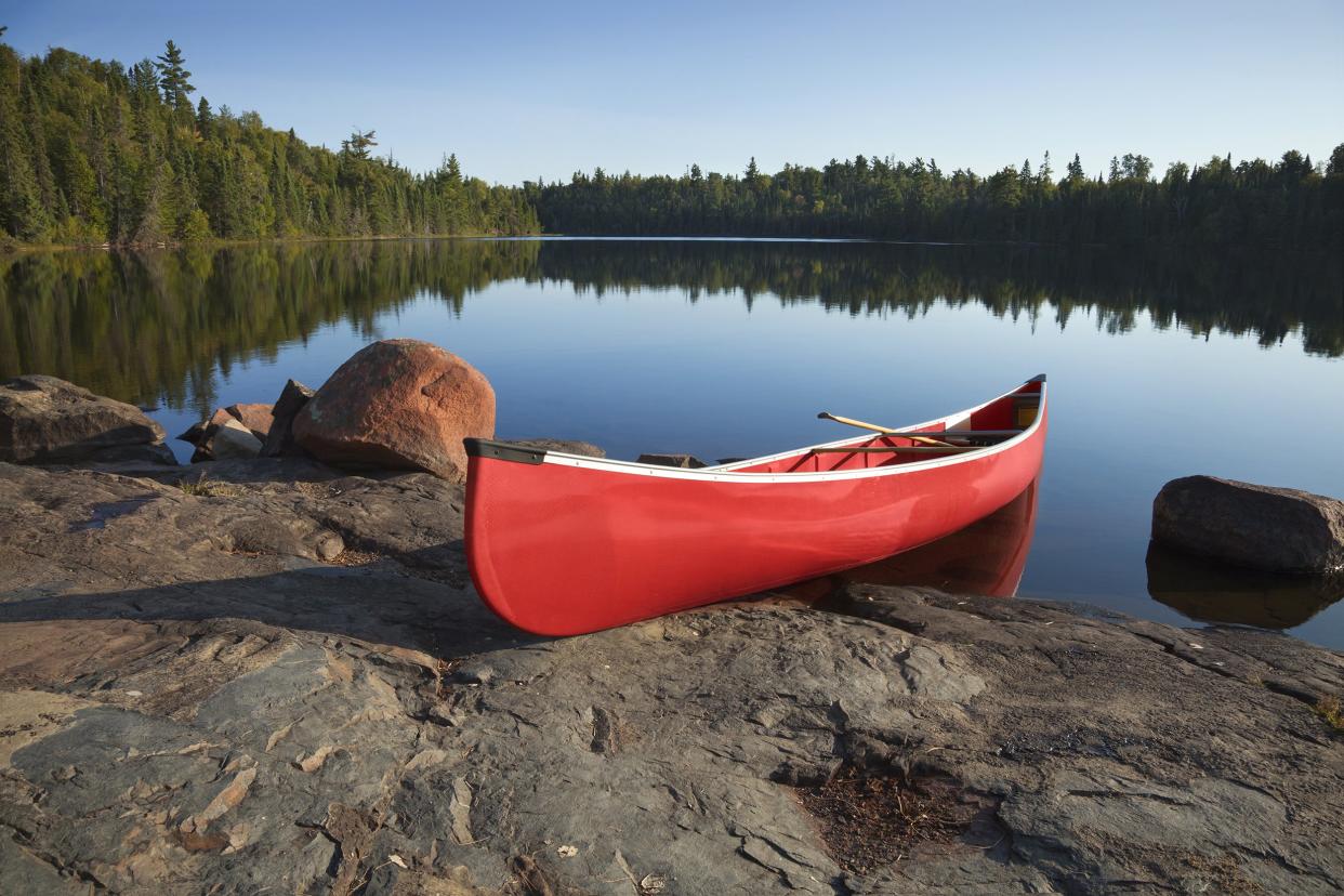 A red canoe rests on a rocky shore of a calm blue lake in Duluth, Minnesota