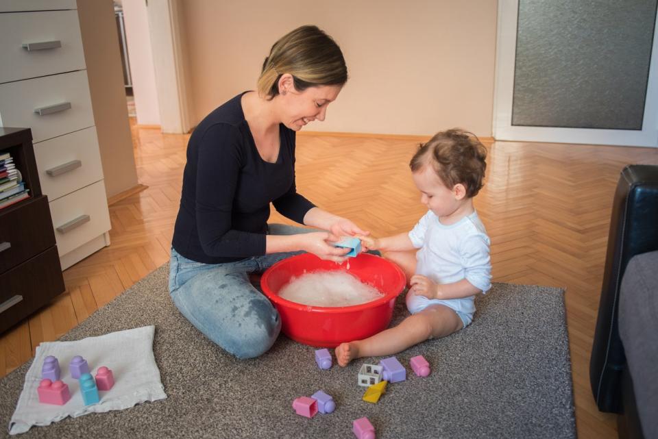 Young mother, woman, washing toys with her toddler son in a living room. 