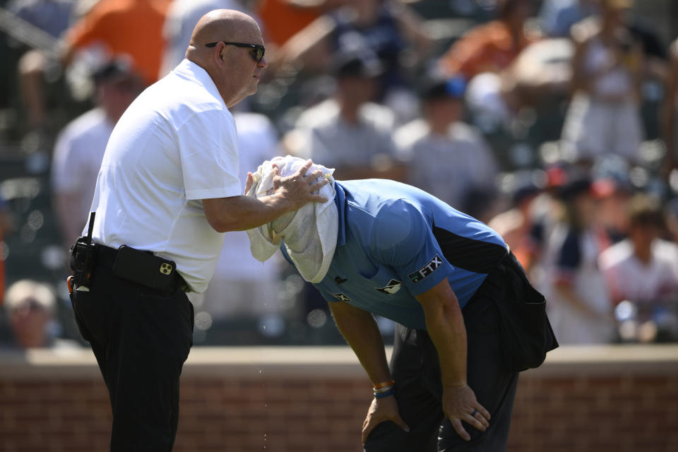 Baltimore Orioles head trainer Brian Ebel, left, helps home plate umpire Scott Barry get relief with a wet towel around his head after the sixth inning of a baseball game between the Orioles and the New York Yankees, Sunday, July 24, 2022, in Baltimore. The Yankees won 5-0. (AP Photo/Nick Wass)