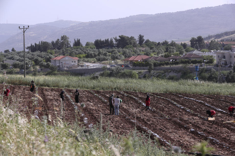 The Israeli village of Metulla, background, is seen from the Lebanese-Israeli border as Syrian farmers work in the village of Kfar Kila, in southeast Lebanon, Wednesday, May 20, 2020. Twenty years after Hezbollah guerrillas pushed Israel's last troops from southern Lebanon, both sides are gearing up for a possible war that neither seems to want. (AP Photo/Bilal Hussein)