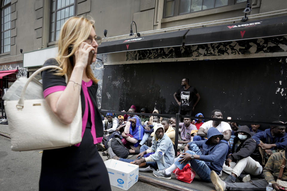 Migrants sit in a queue outside of The Roosevelt Hotel that is being used by the city as temporary housing, Monday, July 31, 2023, in New York. (AP Photo/John Minchillo)