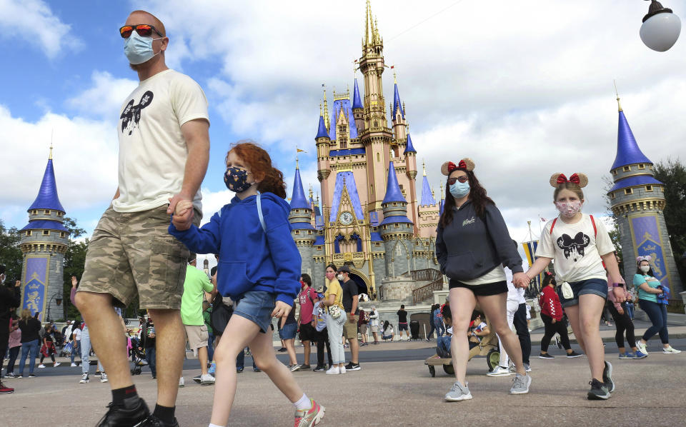 FILE - IN this Dec. 21, 2020 file photo, A family walks past Cinderella Castle in the Magic Kingdom, at Walt Disney World in Lake Buena Vista, Fla. To help celebrate the 50th anniversary of the opening of Walt Disney World in Florida, Mickey and Minnie are getting flashier threads and iconic structures such as Cinderella's Castle and the Tower of Terror are getting new lighting. Disney officials on Friday, Feb. 19, 2021, unveiled the first details on how Disney World will celebrate its milestone anniversary.(Joe Burbank/Orlando Sentinel via AP, File)