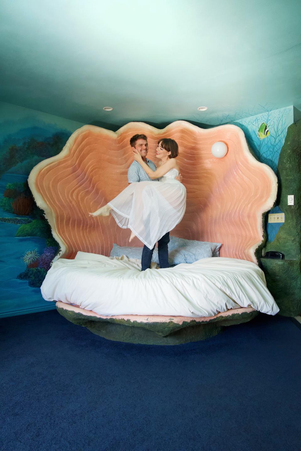 Waukesha native Margaret Bienert and husband, Corey Bienert, pose for a picture on a shell-shaped bed in a themed suite in the Black Swan Inn of Pocatello, Idaho. The pair runs A Pretty Cool Hotel Tour, which explores niche romance hotels across the United States.