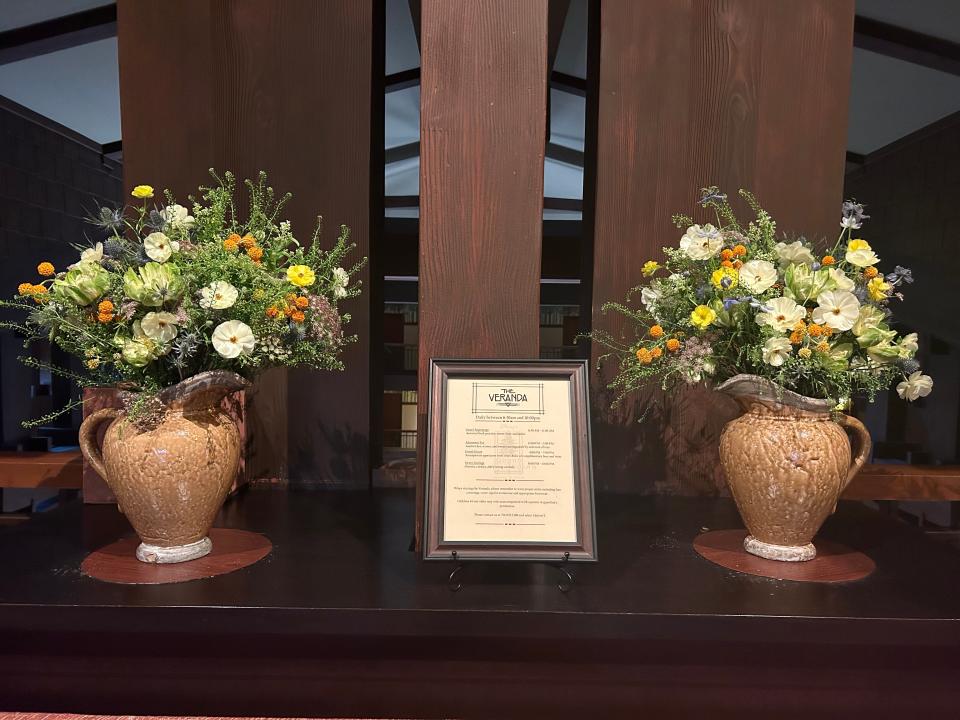 Two large floral arrangements with a framed menu in between.