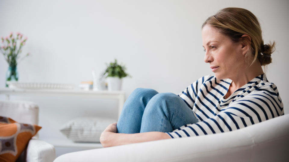 A woman in a striped shirt sitting on a chair hugging her knees as she deals with seasonal affective disorder