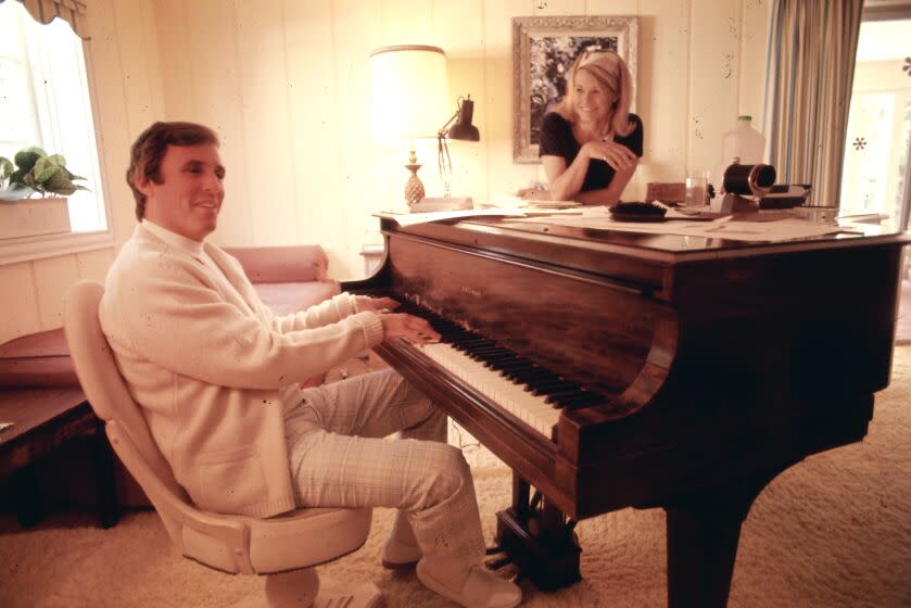 Composer Burt Bacharach plays the piano in his Hollywood home in 1969 while his wife actress Angie Dickinson stands by.