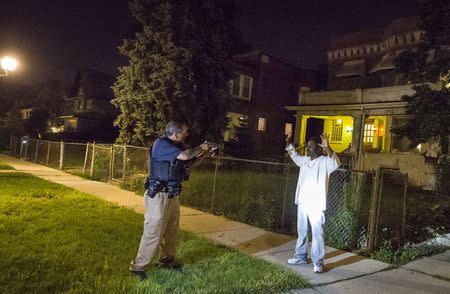 A Cook County Sheriff police officer (L) points his gun at a man who walked up to him while officers were conducting an unrelated street stop in the Austin neighborhood in Chicago, Illinois, United States, September 9, 2015. REUTERS/Jim Young