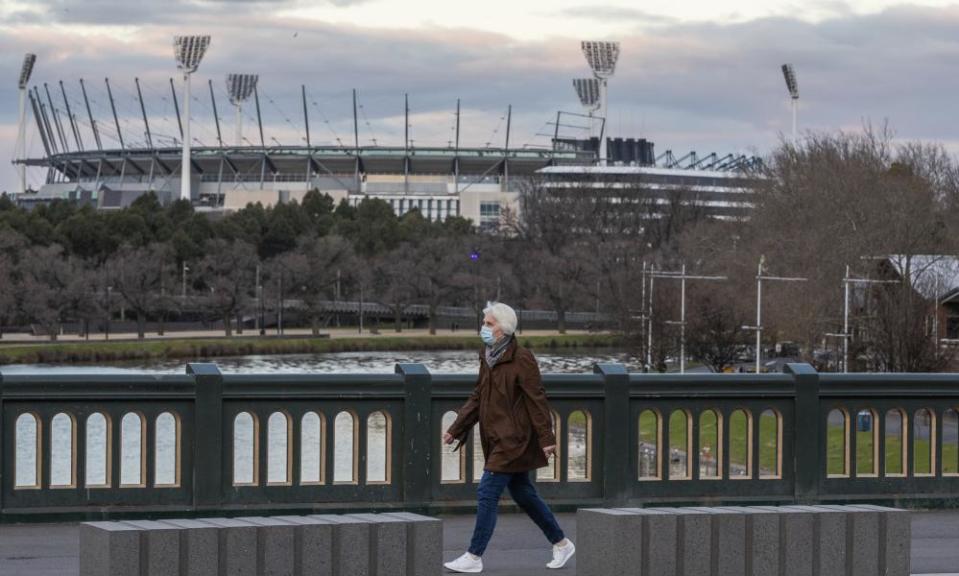 A woman wearing a mask walks along a bridge as she walks past the MCG