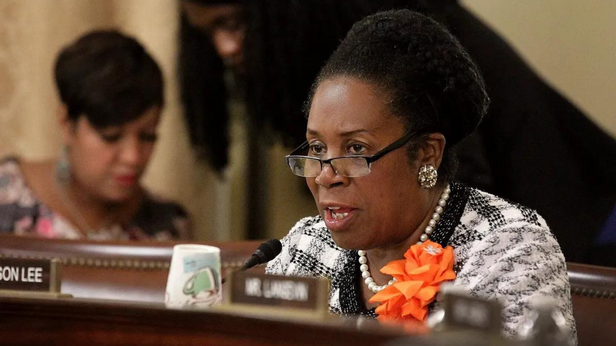 A Black woman speaks into a mic while sitting at a desk. 