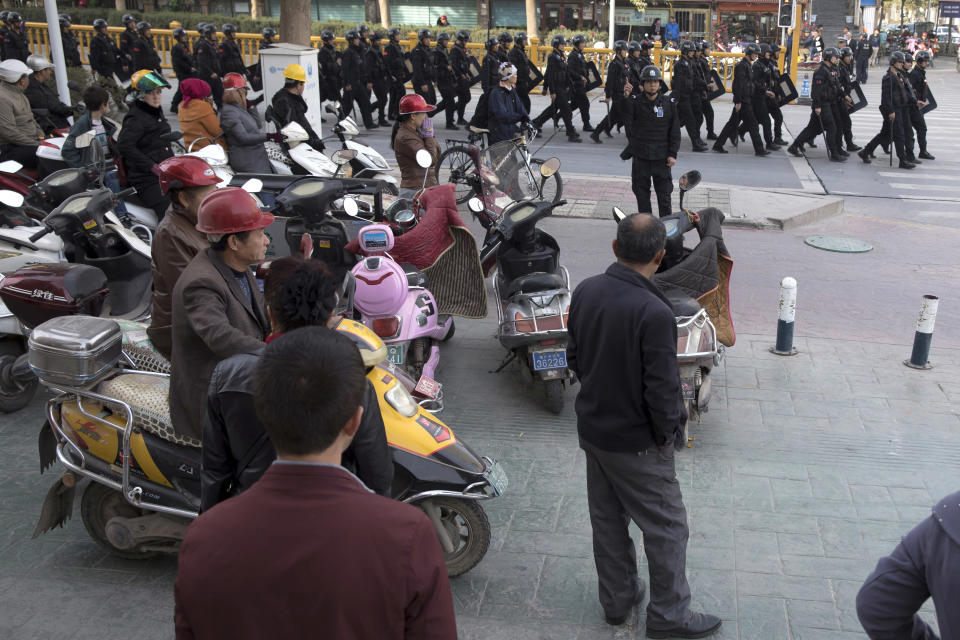 FILE - In this Nov. 5, 2017, file photo, residents watch a convoy of security personnel in a show of force through central Kashgar in western China's Xinjiang region. A Chinese Communist Party official signaled Monday, Dec. 21, 2020 that there would likely be no let-up in its crackdown in the Xinjiang region, but said the government's focus is shifting more to addressing the roots of extremism. (AP Photo/Ng Han Guan, File)