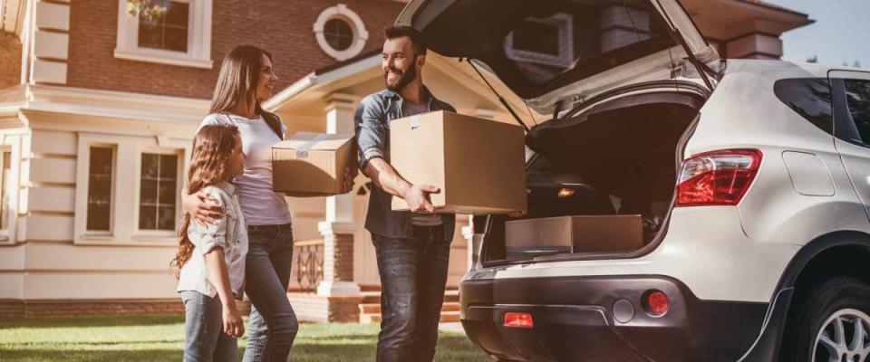 Happy family is standing near car with cardboard boxes. Moving day.