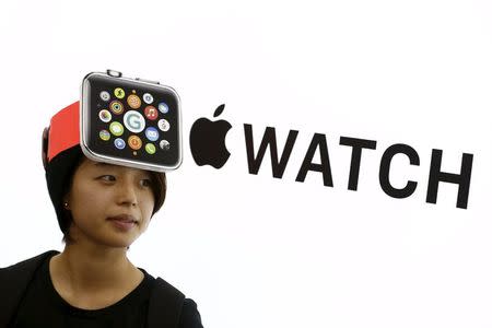 A woman wearing a mock-up of an Apple Watch stands in front of an Apple sign at an electronics store in Tokyo April 24, 2015. REUTERS/Thomas Peter