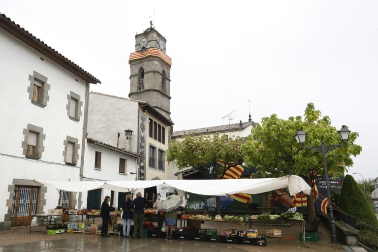 People buy vegetables and fruits at a street market close to the church's bell tower decorated with a Catalan flag in the village of l'Esquirol