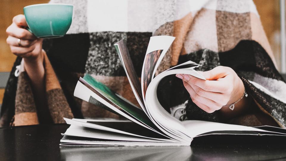 Girl are sitting in the coffee shop with cup of coffee and reading book or magazine.