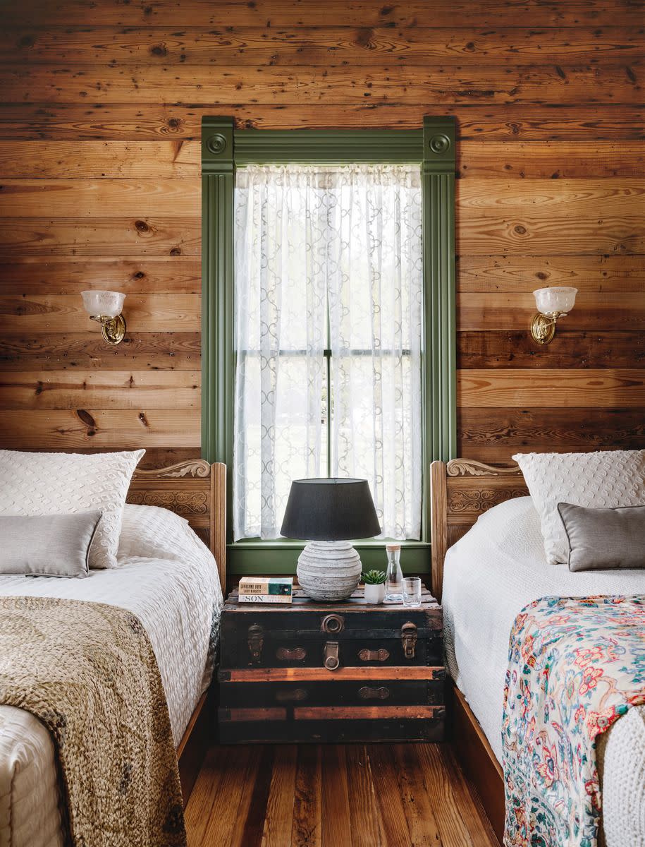 pine shiplap walls in a bedroom that has two twin sized beds and a window in the middle with lace curtains