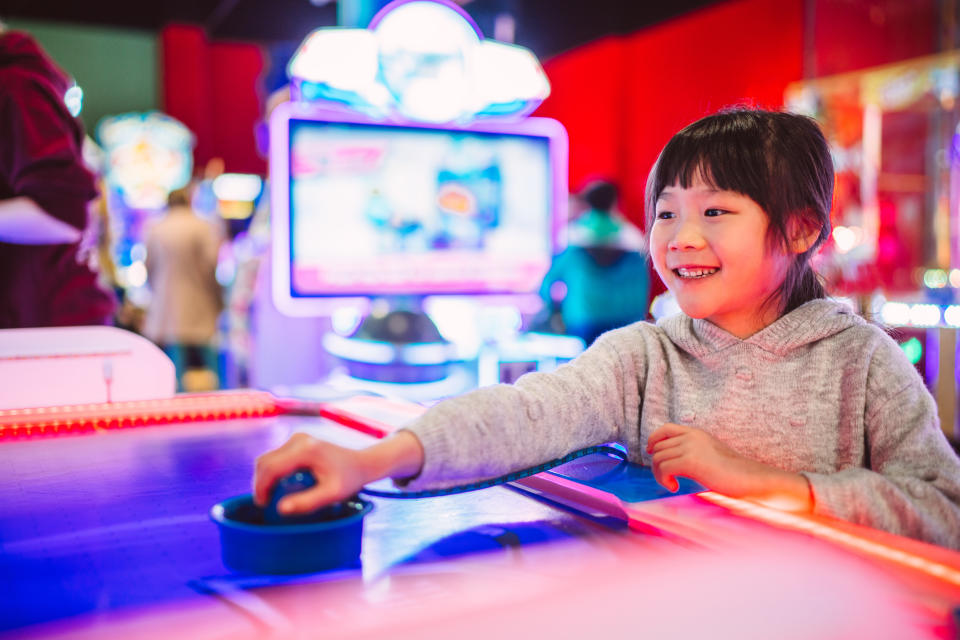 Lovely cheerful girl enjoying playing air hockey with friend at amusement arcade.