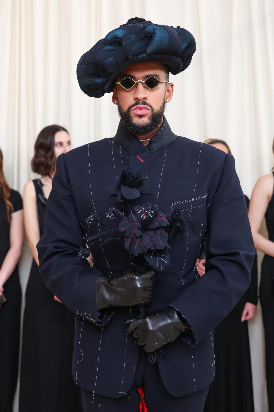 Bad Bunny in a unique hat and structured jacket with embellishments, standing confidently