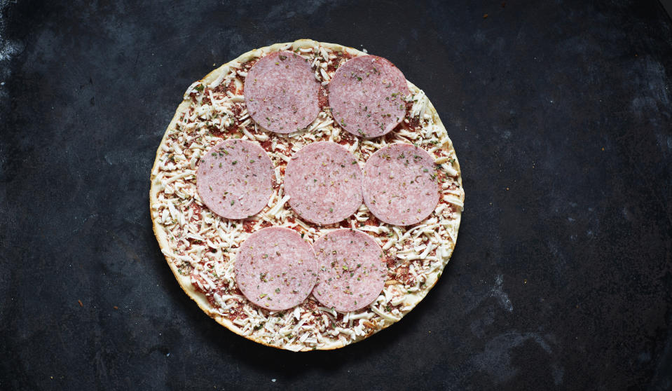 Frozen pizza with salami and grated cheese