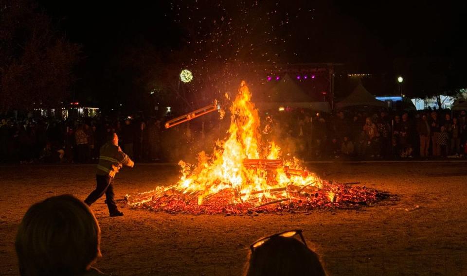 A firefighter throws a pallet onto the giant bonfire at Paso Robles’ New Year’s Eve celebration in the Downtown City Park on Dec. 31, 2023.