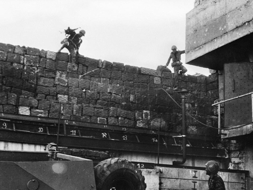 A black and white photo of Syrian Soldiers jumping over a wall.