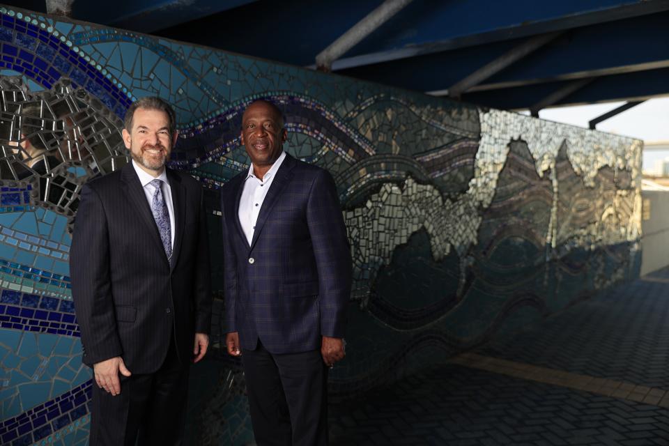 On Jacksonville's Southbank, Jewish Community Alliance CEO Adam Chaskin (left) and First Coast YMCA President and CEO Eric Mann pose in front of  Kate Garcia Rouh's mosaic art, "Mirrored River: Where do you see yourself?" The two CEOs have spearheaded a unity initiative to encourage community members to embrace each other's differences.