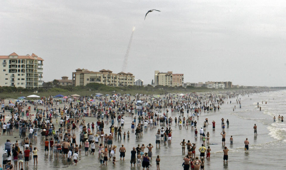 FILE - In this Friday, July 8, 2011 file photo, crowds gather in the surf and on the beach in Cocoa Beach, Fla., to watch the launch of the space shuttle Atlantis on STS-135. This is the final U.S. shuttle mission before the fleet is retired. In ordinary times, the beaches and roads along Florida’s Space Coast would be packed with hundreds of thousands of spectators, eager to witness the first astronaut launch from Florida in nine years, scheduled for May 27, 2020. In the age of coronavirus, local officials and NASA are split on whether that's a good idea. (AP Photo/Dave Martin)