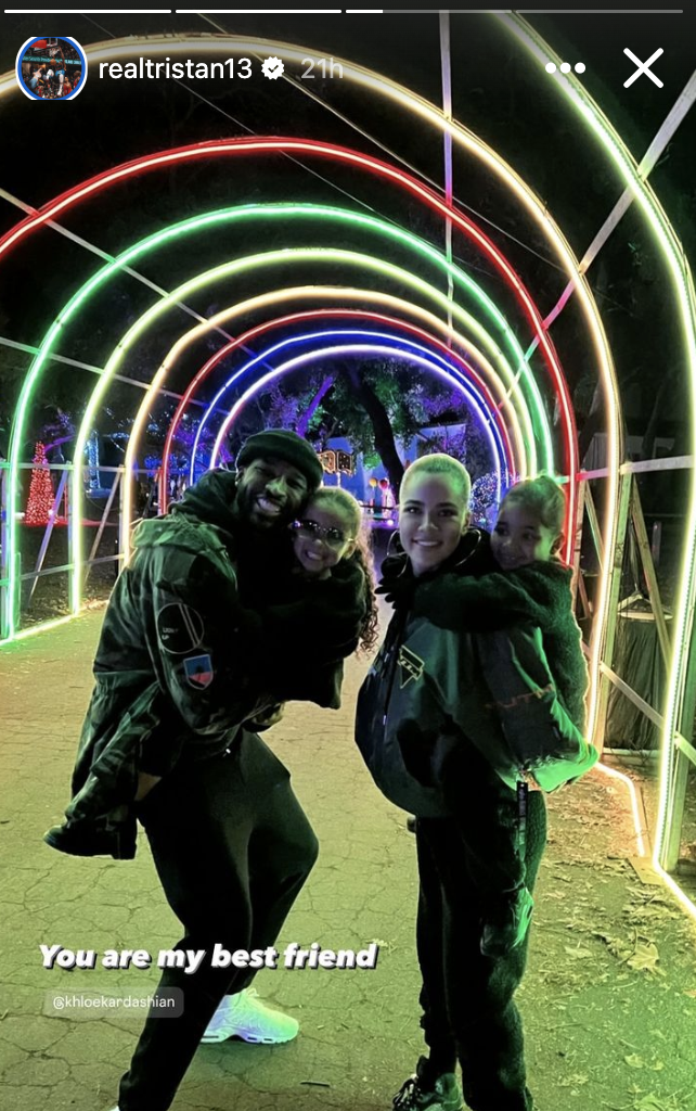 Tristan Thompson and Khloe Kardashian smile while carrying their children, posing under a festive LED archway. Text reads, "You are my best friend" with a mention of Khloe Kardashian