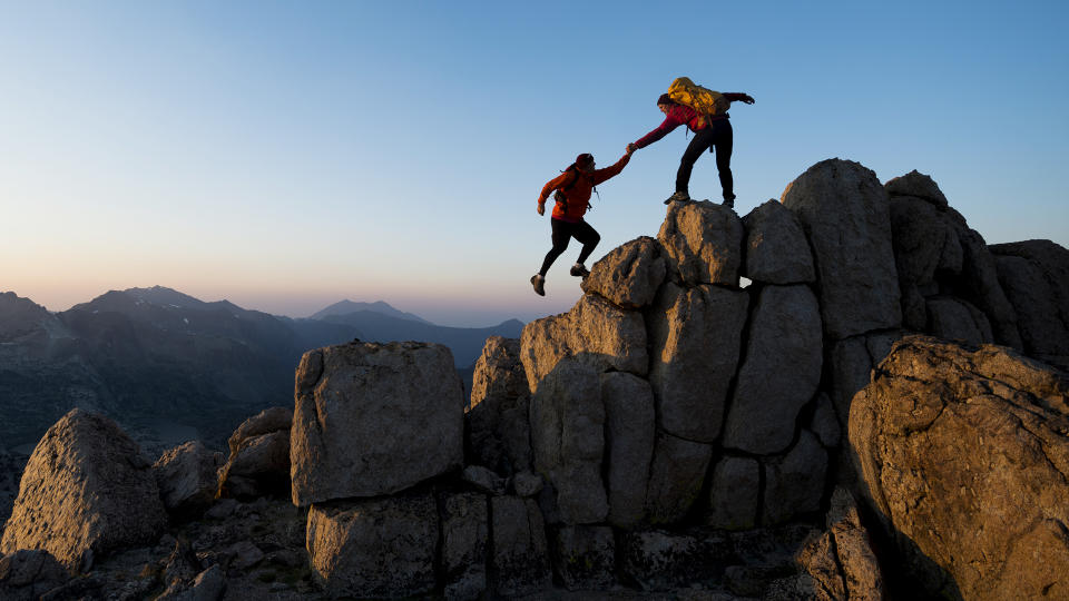 One climber helping the other get to the top of a mountain .