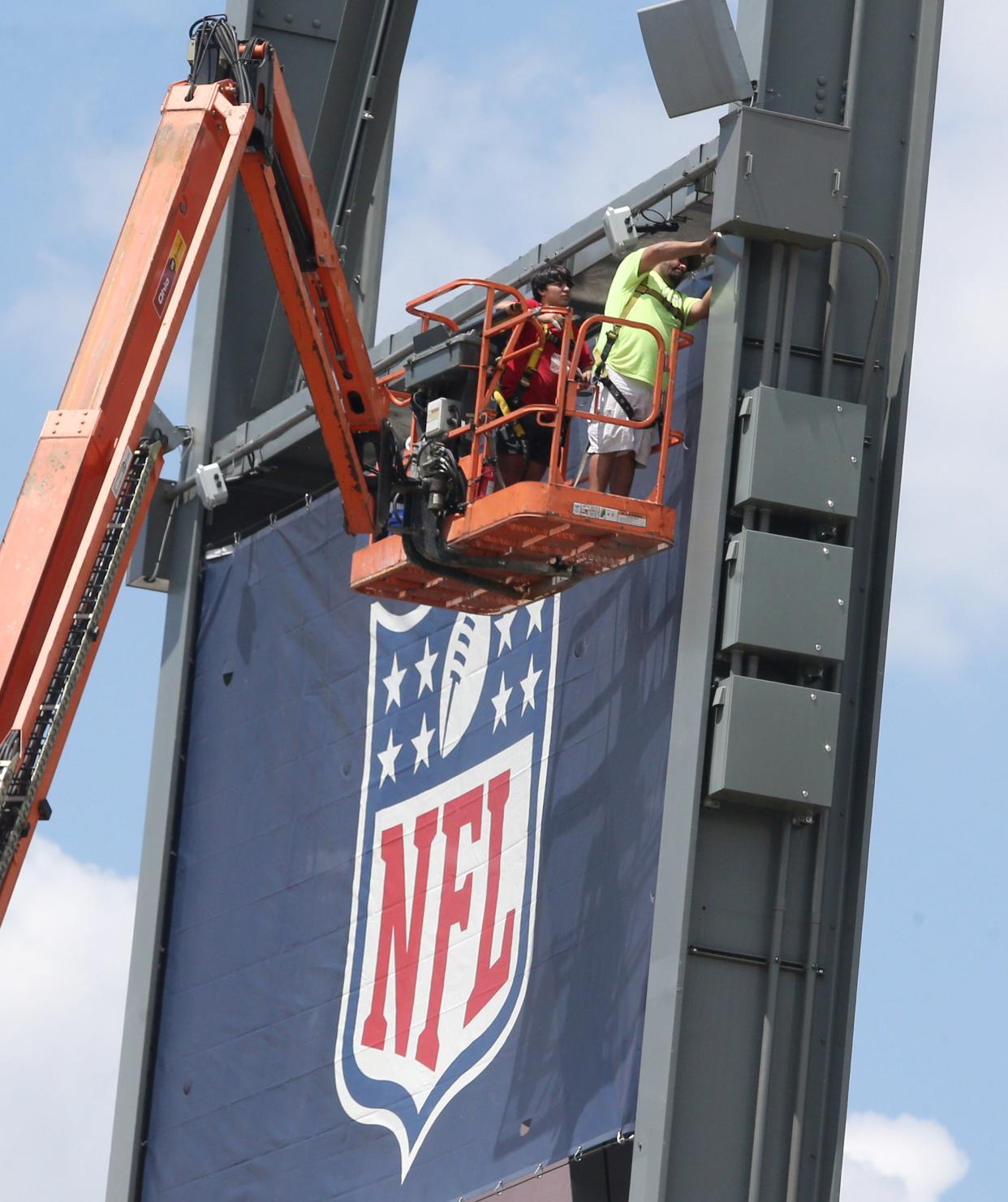 Banners are secured to light standards July 14 at Tom Benson Hall of Fame Stadium in preparation for Enshrinement Week in Canton.