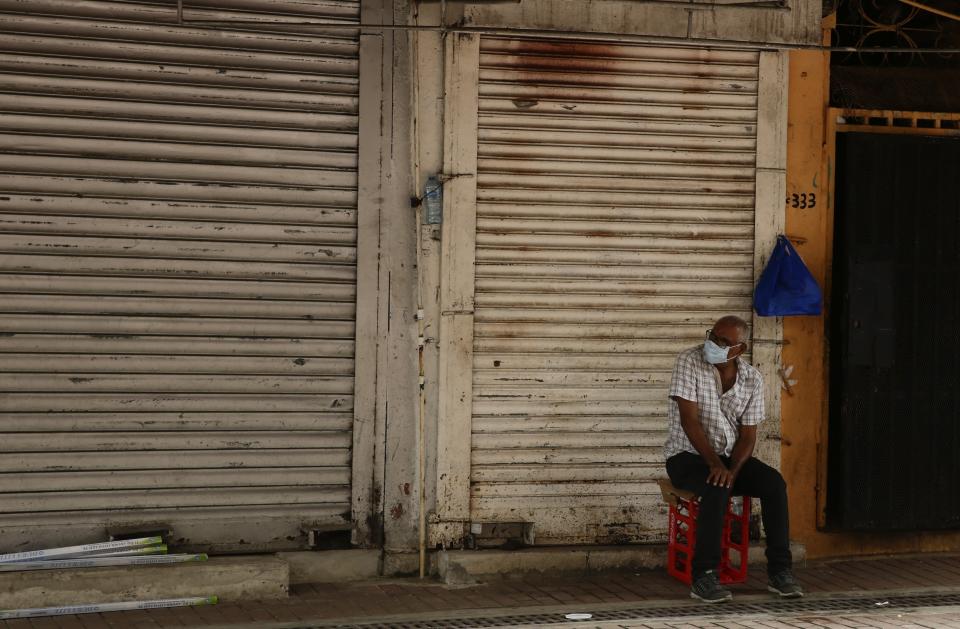 Un hombre con una mascarilla para protegerse del nuevo coronavirus se sienta afuera de una tienda de comestibles cerrada en el centro de la Ciudad de Panamá, el martes 14 de julio de 2020. El país centroamericano vive un repunte sostenido de los casos de COVID-19 que tiene al gobierno evaluando endurecer el confinamiento en la capital y otras zonas con los mayores contagios. (AP Foto/Arnulfo Franco)