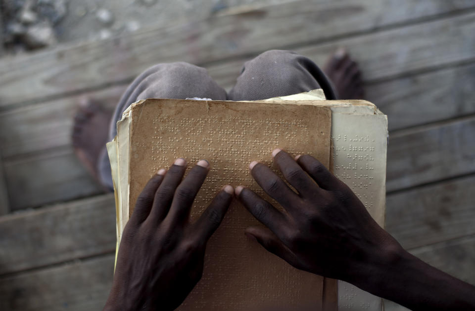 In this picture taken on Feb. 15, 2012, Joseph Clodise, 25, with visual disabilities reads in Braille at the entrance of his home at La Piste camp in Port-au-Prince, Haiti. While more than a million people displaced by the 2010 quake ended up in post-apocalyptic-like tent cities, some of the homeless people with disabilities landed in the near-model community of La Piste, a settlement of plywood shelters along tidy gravel lanes. However, the rare respite for the estimated 500-plus people living at the camp is coming to an end as the government moves to reclaim the land. (AP Photo/Ramon Espinosa)