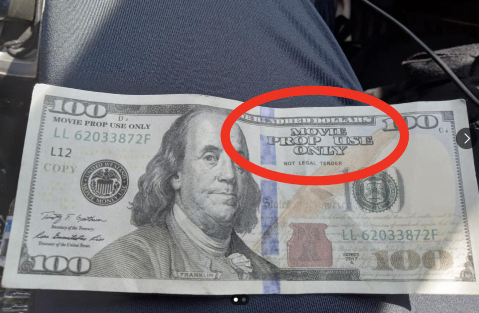 Person holding a fake $100 bill with "MOVIE PROP USE" printed on it