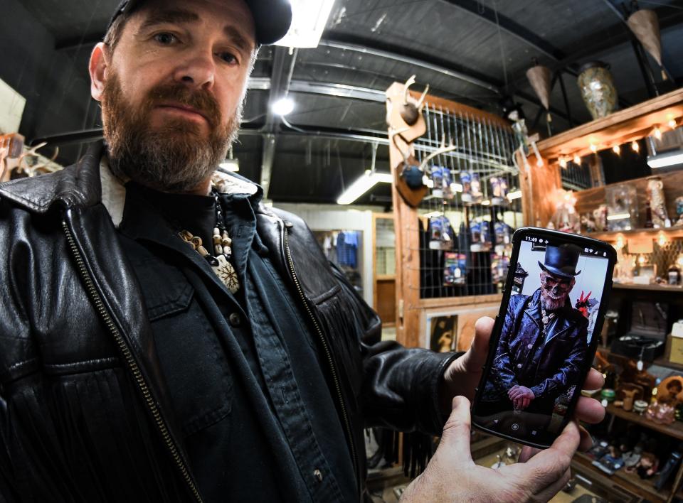 John Harris, who goes by the moniker "Baron Johny Ross" when working as a Voodoo practitioner, shows a portrait of the regalia he wears while providing consultations, Tuesday Jan. 11, 2022, at he and wife Jenifer's newly-opened Voodoo's World of Oddtiques shop in the REO Town Marketplace on South Washington Avenue in Lansing.